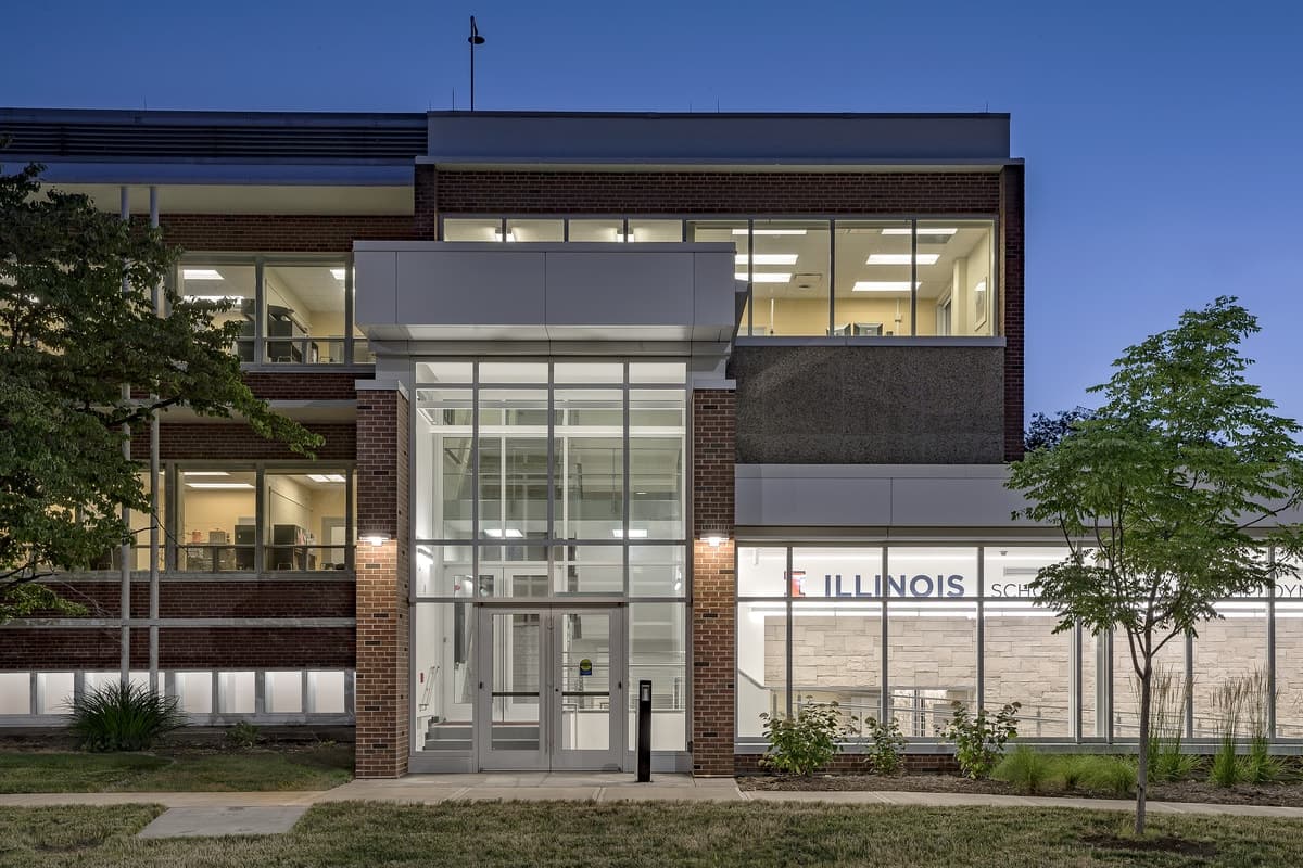 Modern Illinois building with glass entrance and brick facade, surrounded by landscaped greenery.
