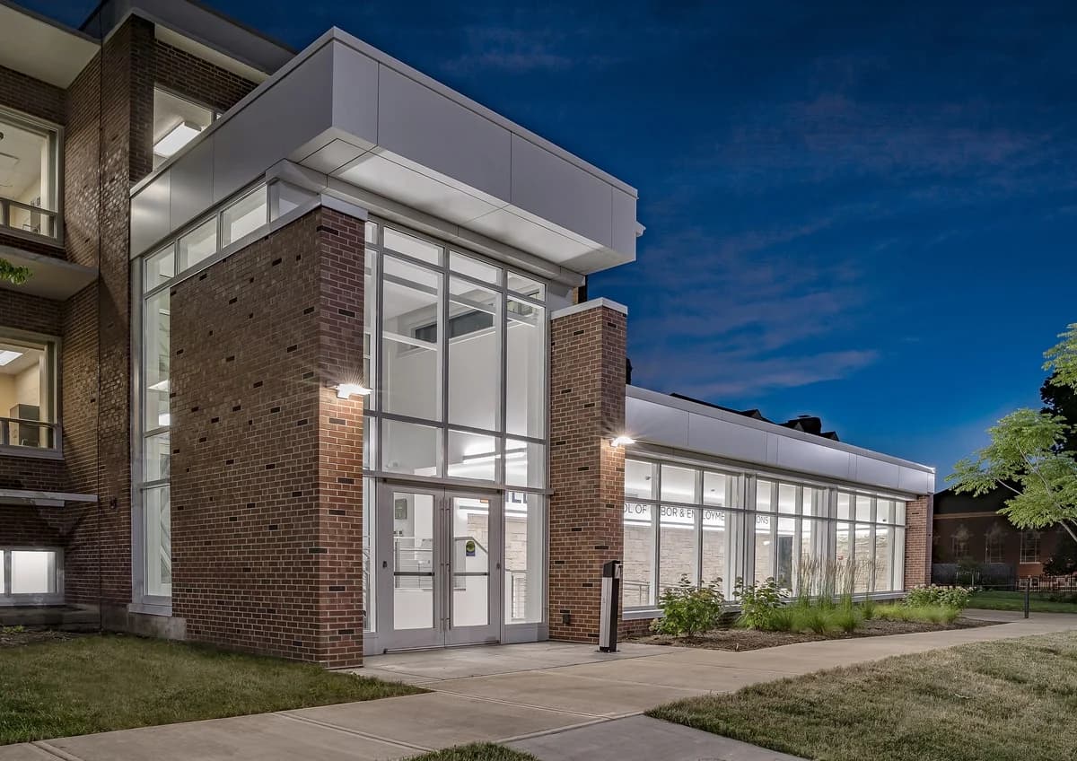 Modern building with brick and glass facade illuminated against an evening sky.