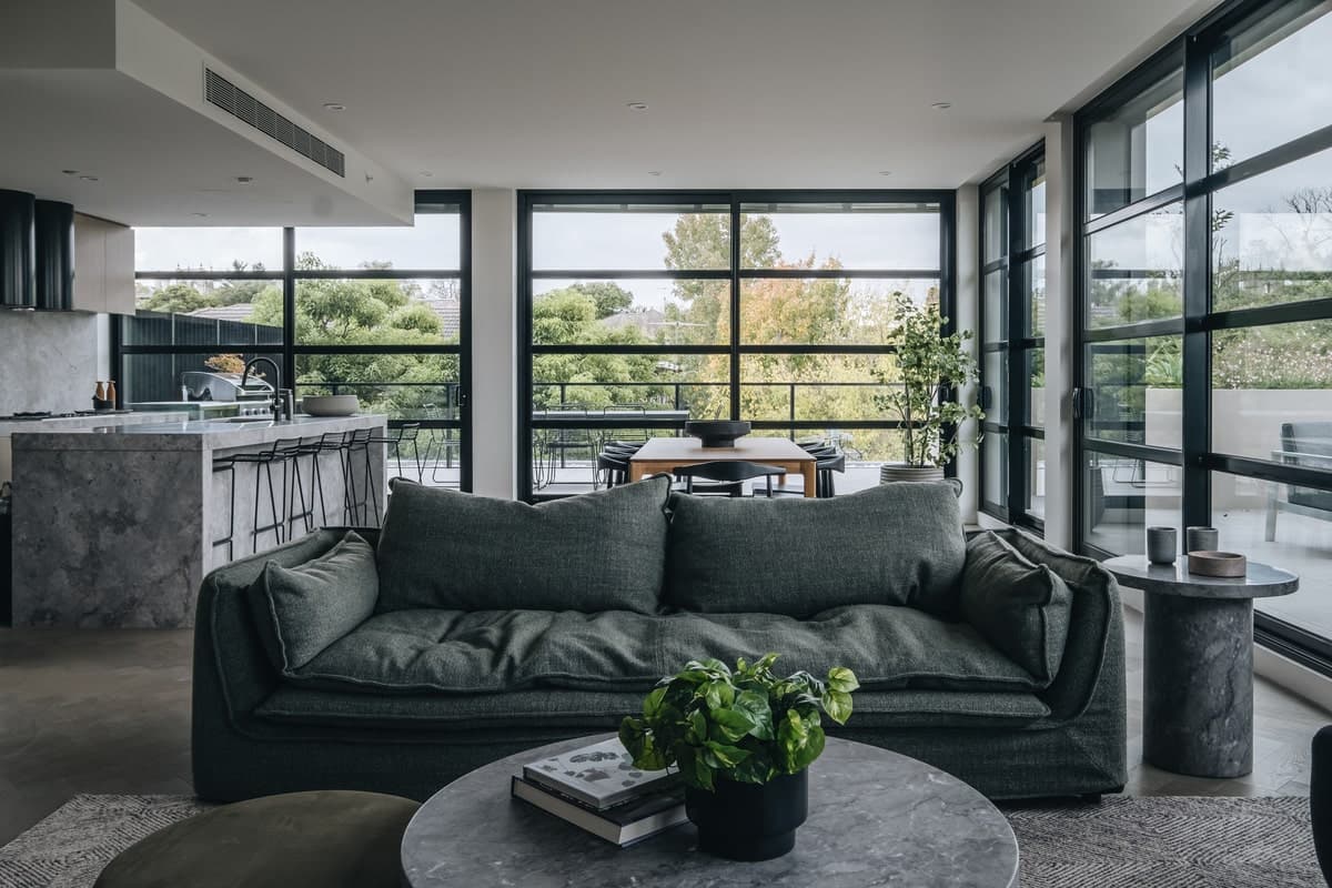 Modern open-concept living space with green sofa, large windows, and minimalist kitchen.