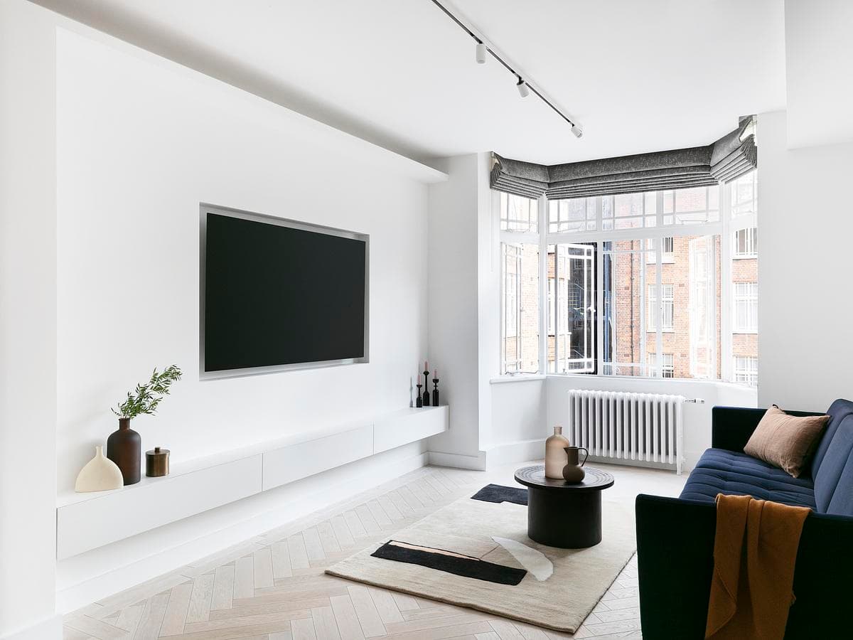 Light-filled living room with a bay window, white media wall and blue sofa at West 5 Apartment.