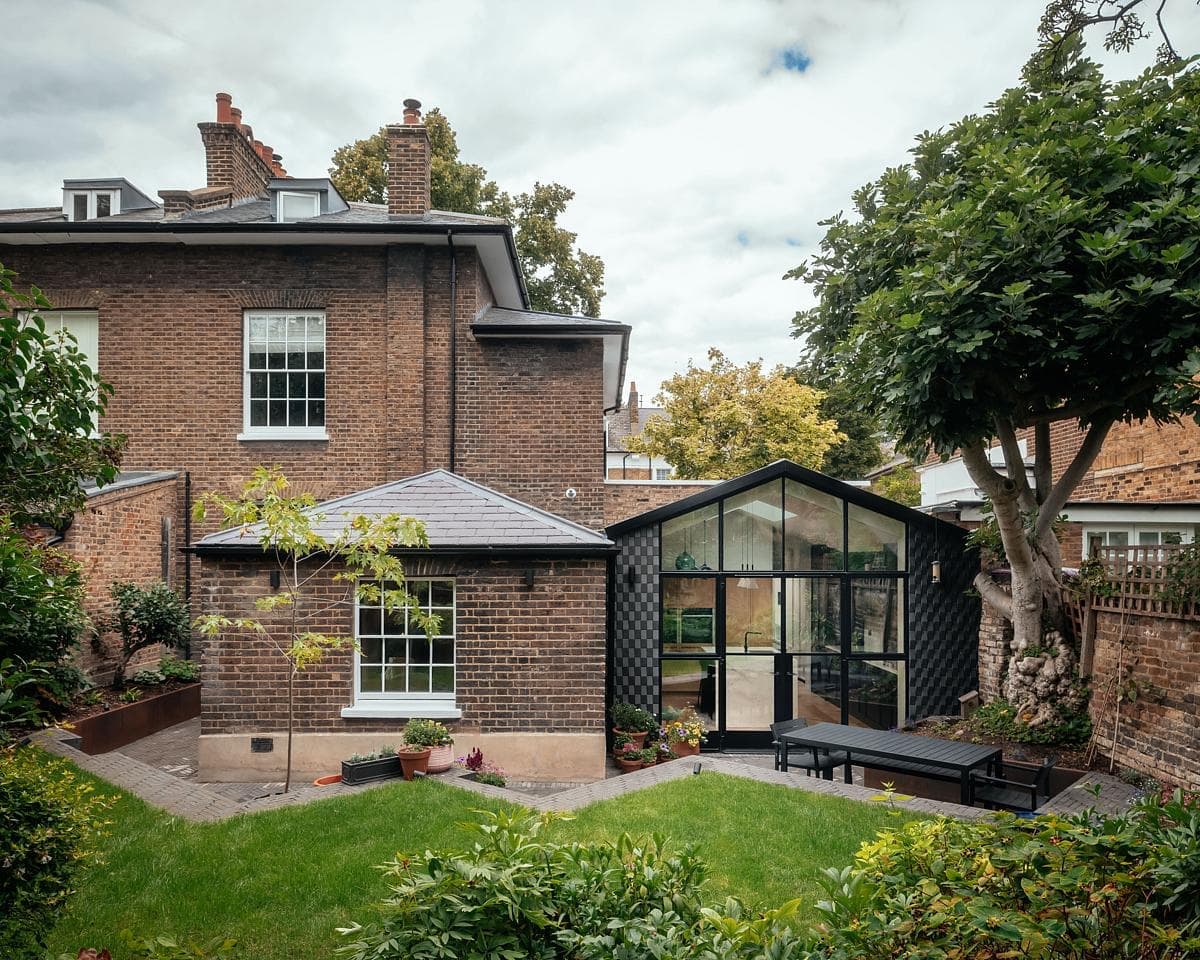 Charming brick house with a modern glass extension in a lush garden setting.