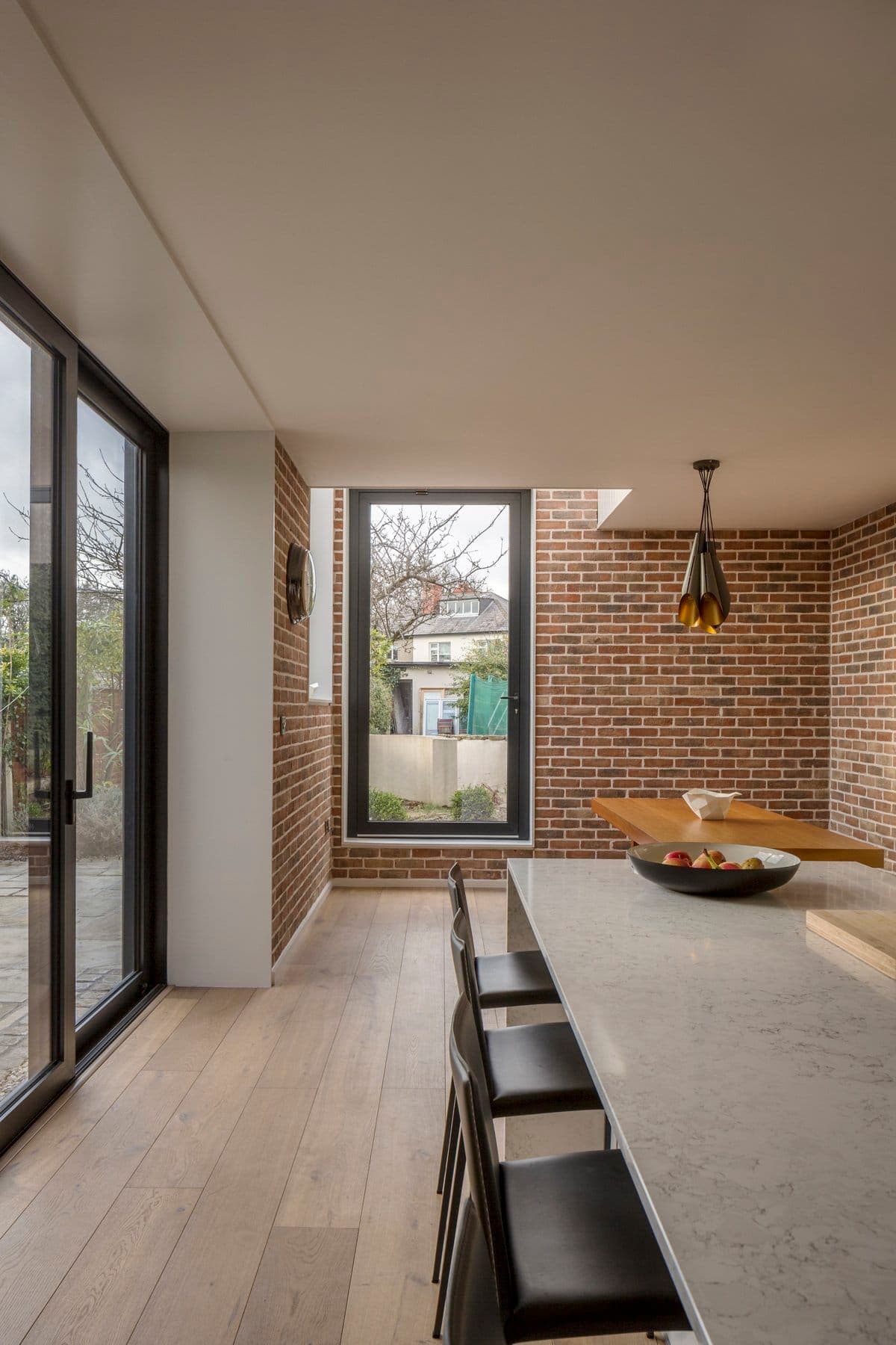Modern dining area with large glass windows, exposed brick walls, and sleek minimalist design.