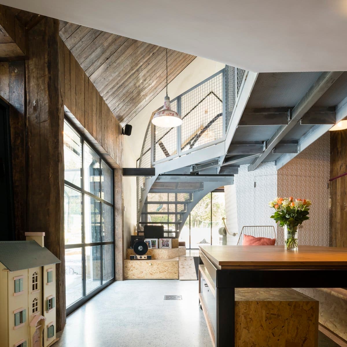 Modern industrial interior with open-plan layout, large windows, and a mix of concrete, metal, and wood.