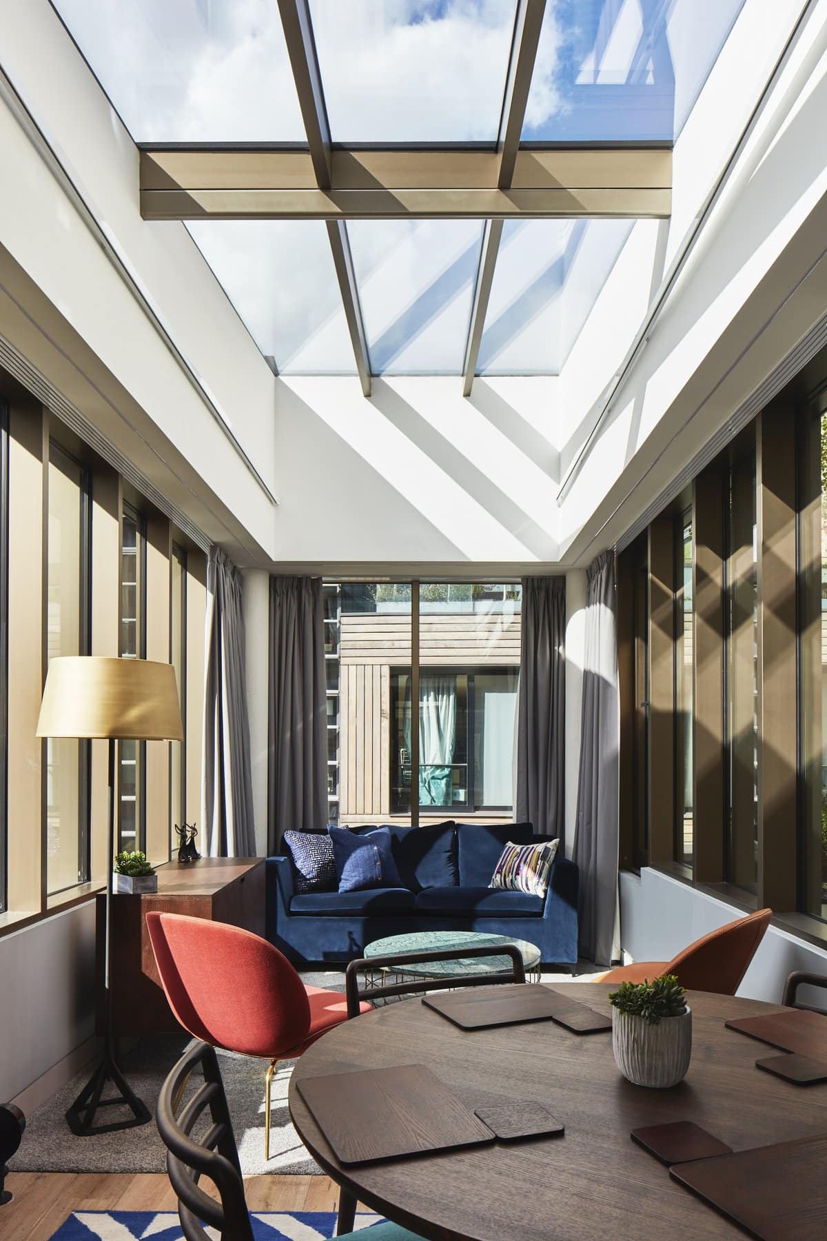 Modern living space with skylight, dark blue sofa, wooden dining table, and vibrant accents.
