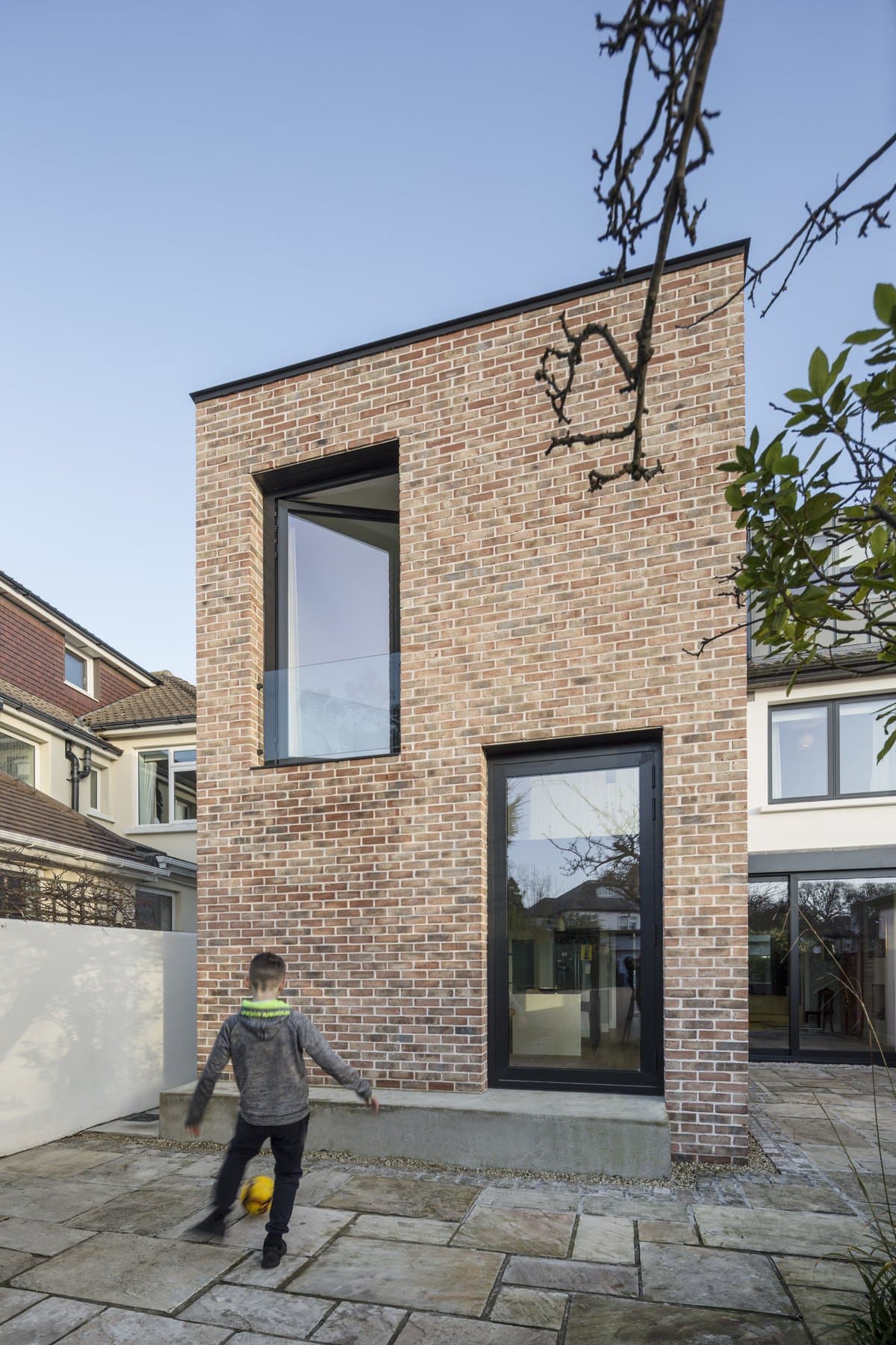 Modern brick house with child playing outside, contrasting traditional homes, late autumn setting.