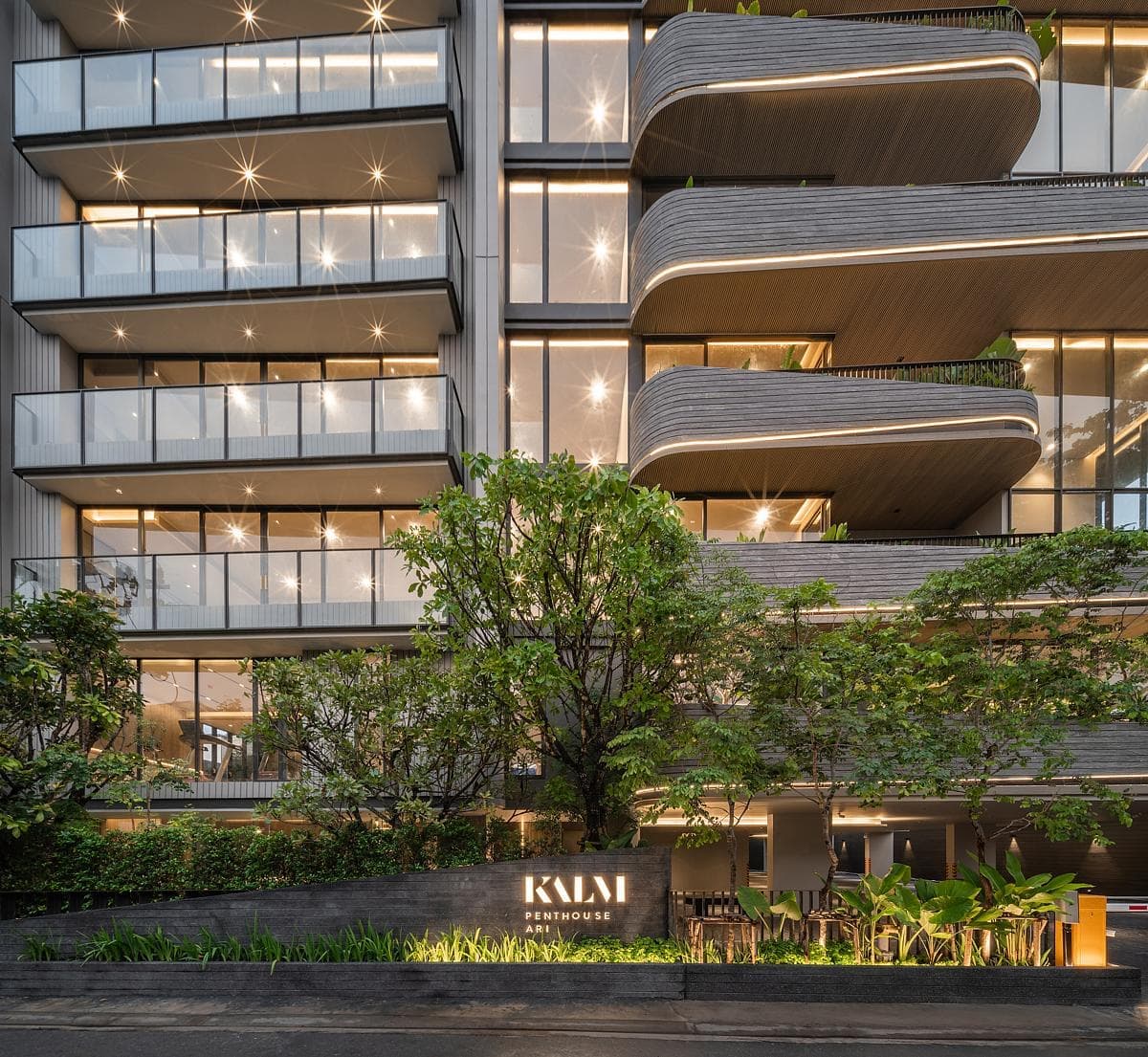 Modern multi-story building with glass balconies and greenery, named KALM Penthouse, elegant urban architecture.