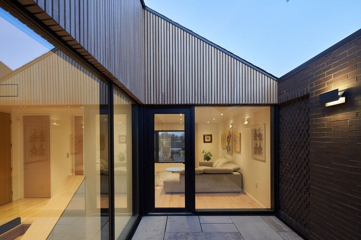 Modern courtyard with large glass windows, brick and wood exterior, and minimalist interior design.