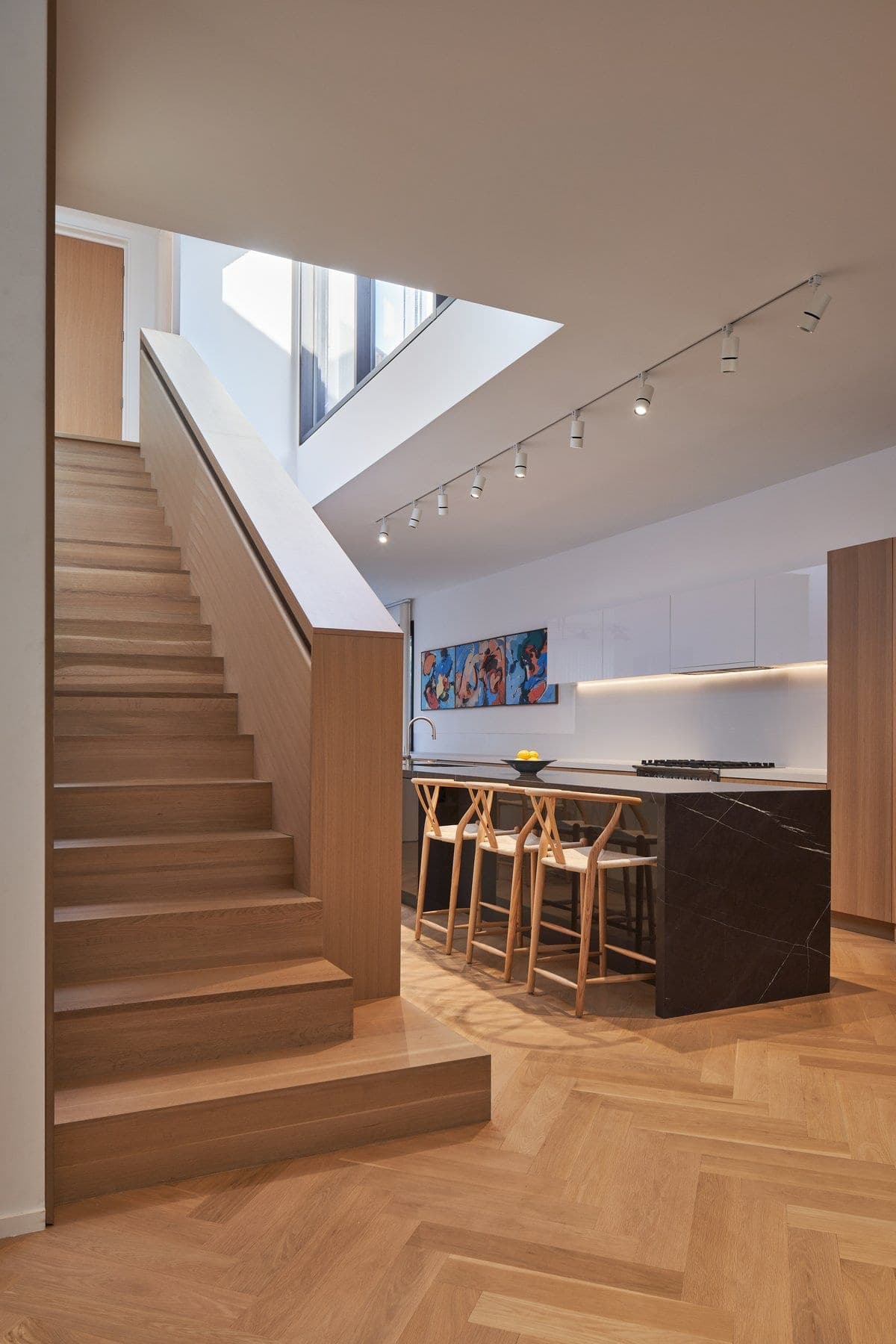 Modern residential interior with wooden stairs, open-plan kitchen, and large artwork.