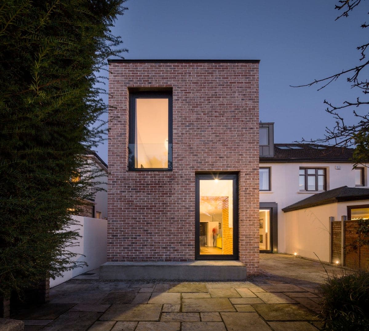 Modern brick house extension with large windows at dusk.