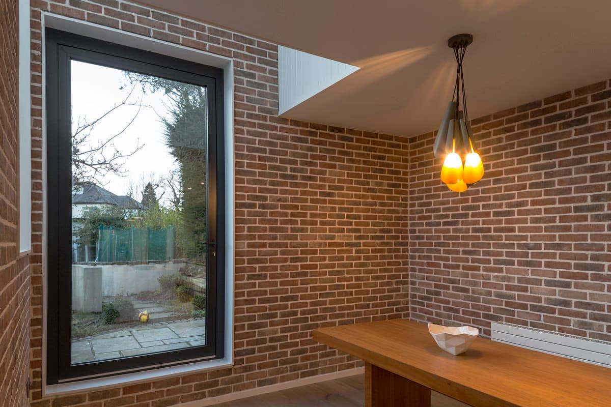 Modern rustic interior with red brick walls, concrete floor, and large window with garden view.