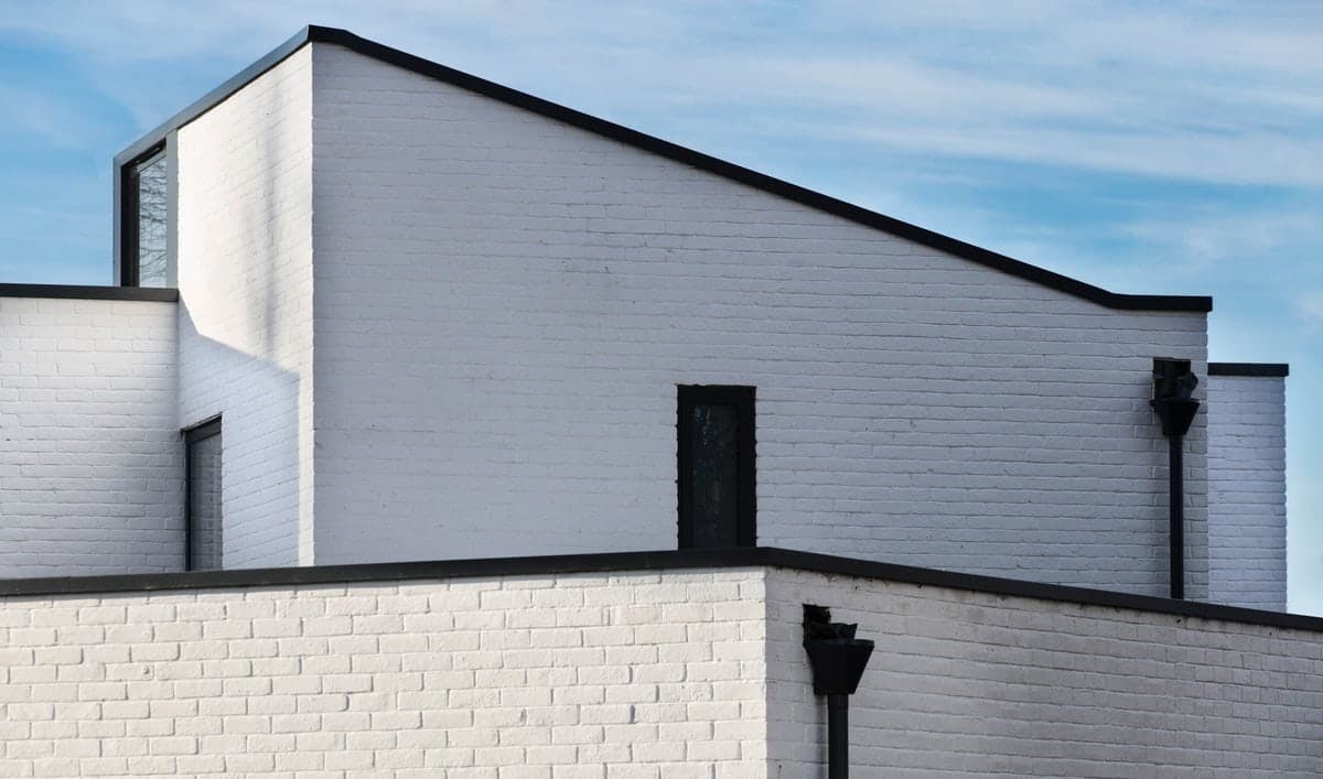 Minimalist white building with geometric shapes and black accents under a clear blue sky.