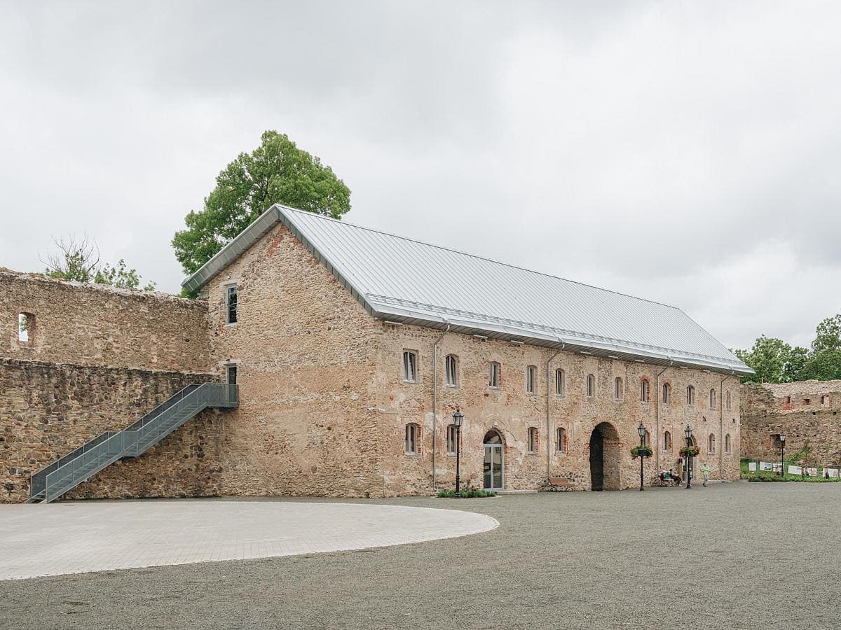 Charming historic stone building with courtyard, archways, and a metal roof under overcast skies.