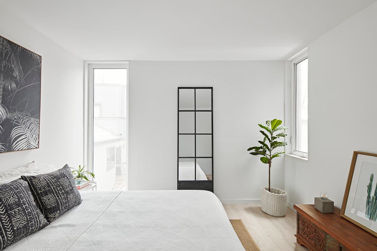Modern, serene bedroom with white linens, abstract art, and natural light from two windows.