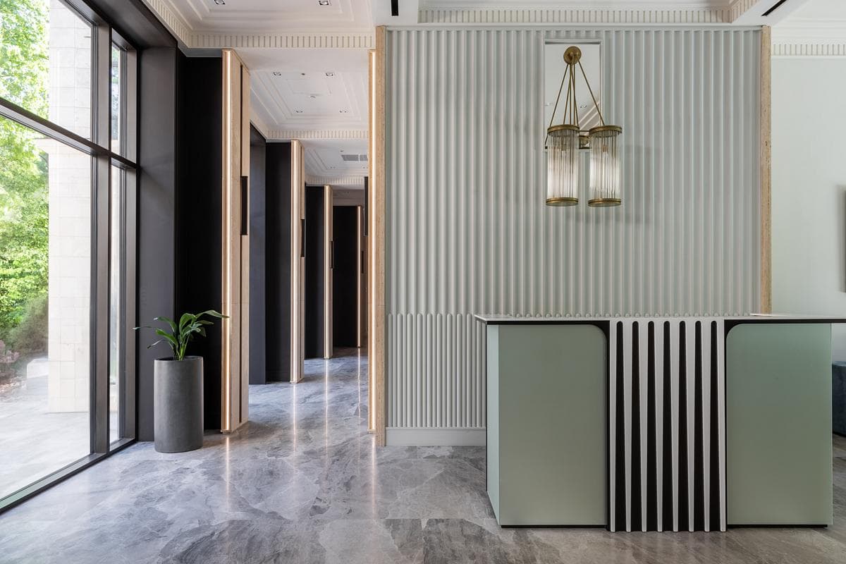 Modern office reception area with pastel green desk, lantern lights, wooden door frames, and marble flooring.