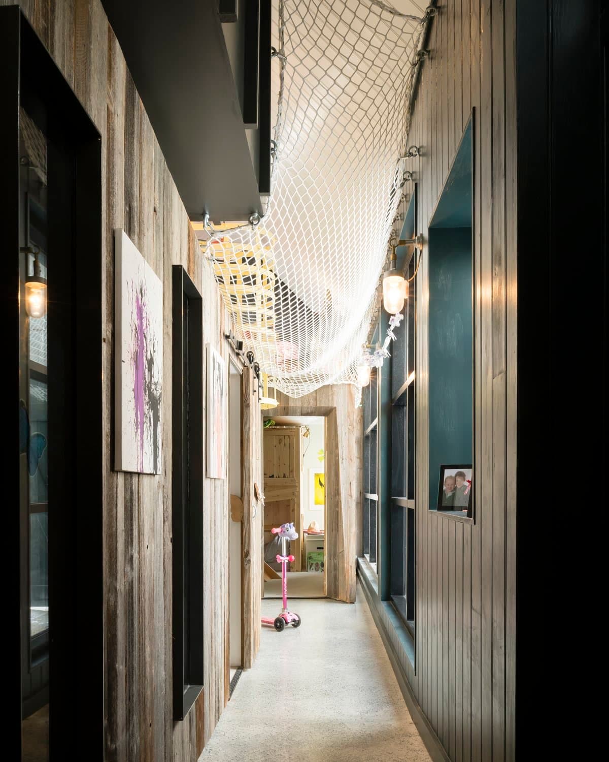 Rustic-modern hallway with wooden panels, concrete flooring, and playful netting. Family-friendly design.