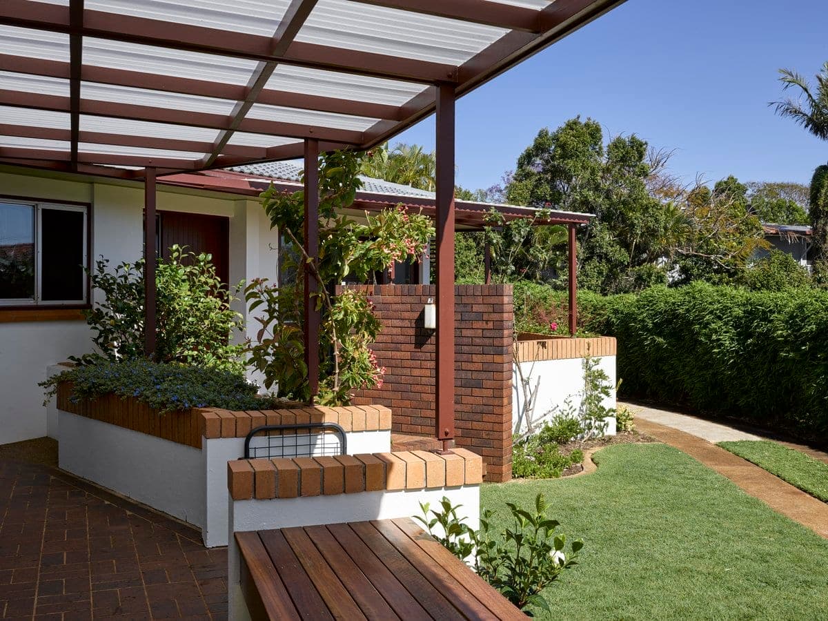 Serene backyard with covered patio, wooden bench, lush garden, and manicured lawn.
