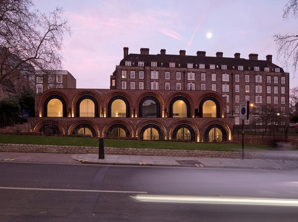 Modern building with illuminated arches at twilight, framed by urban and natural elements.