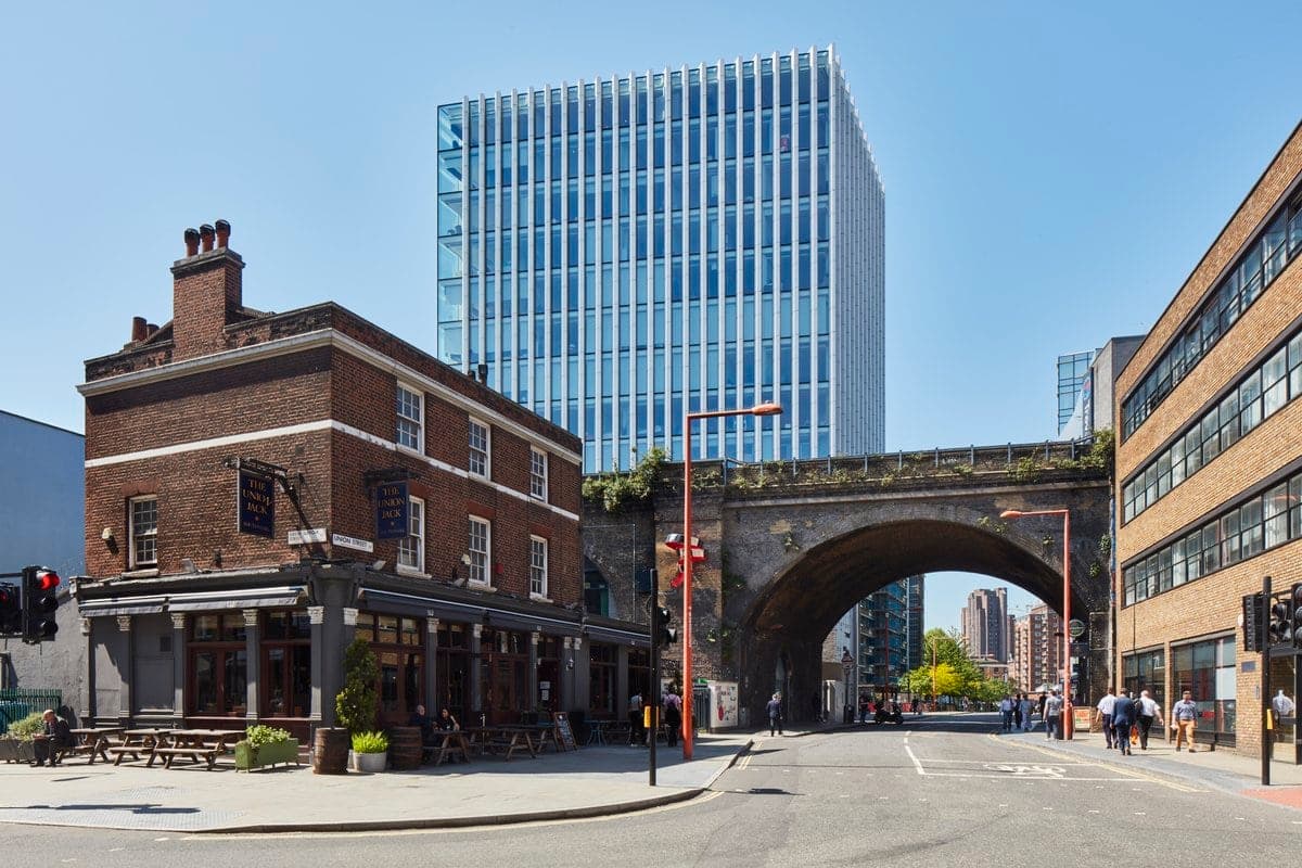 Urban scene with historic brick pub, arched railway bridge, and modern high-rise building.