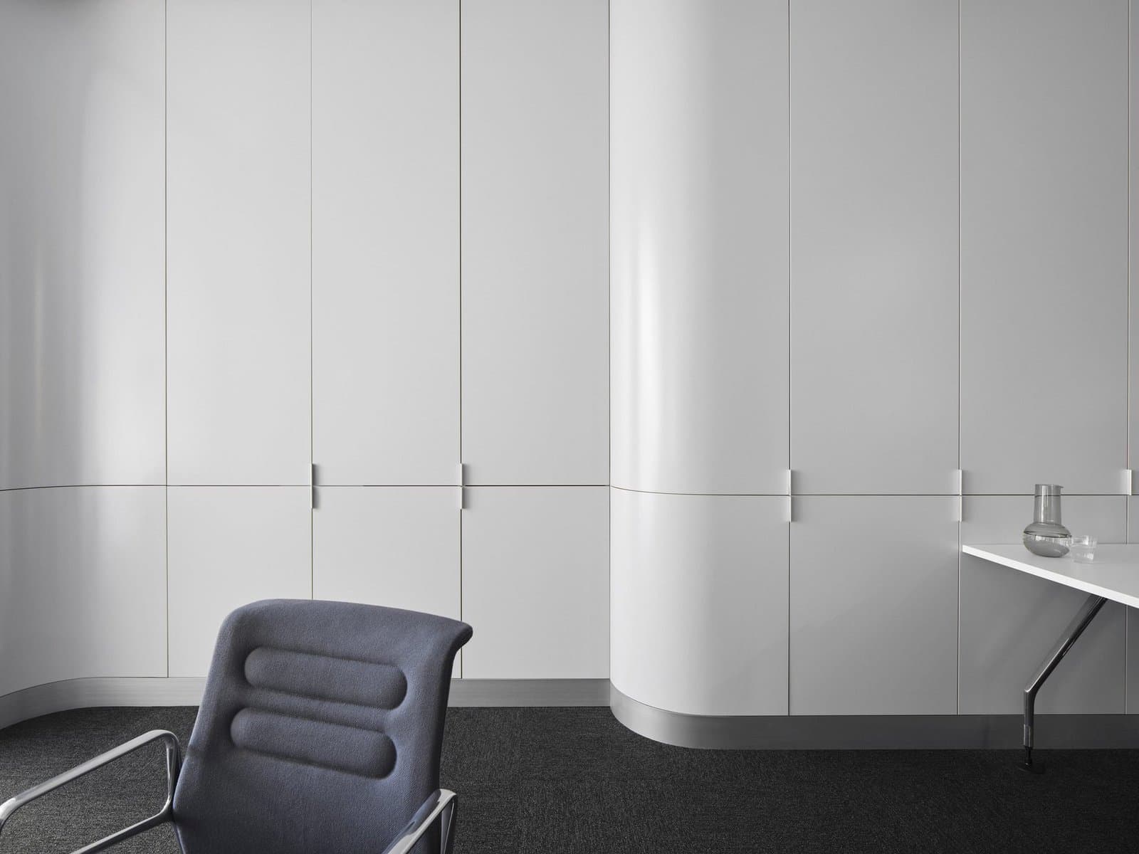 Modern minimalist workspace with white cabinets, dark office chair, and elegant table.