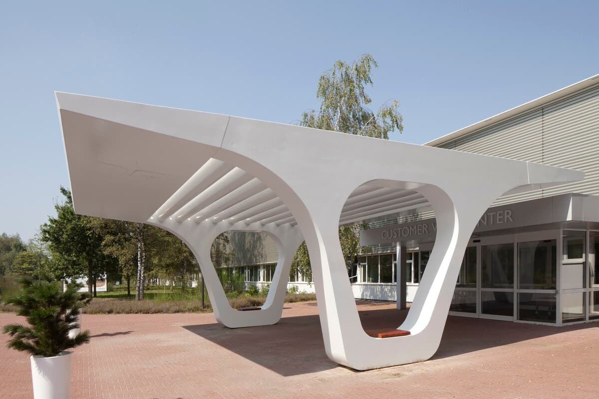 Modern white canopy structure at Experience Center entrance with red brick pathway and greenery.