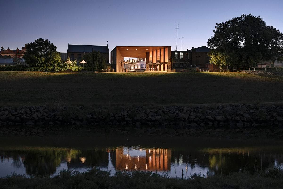 The riverfront pavilion lit at dusk, seen across the Hunter River.
