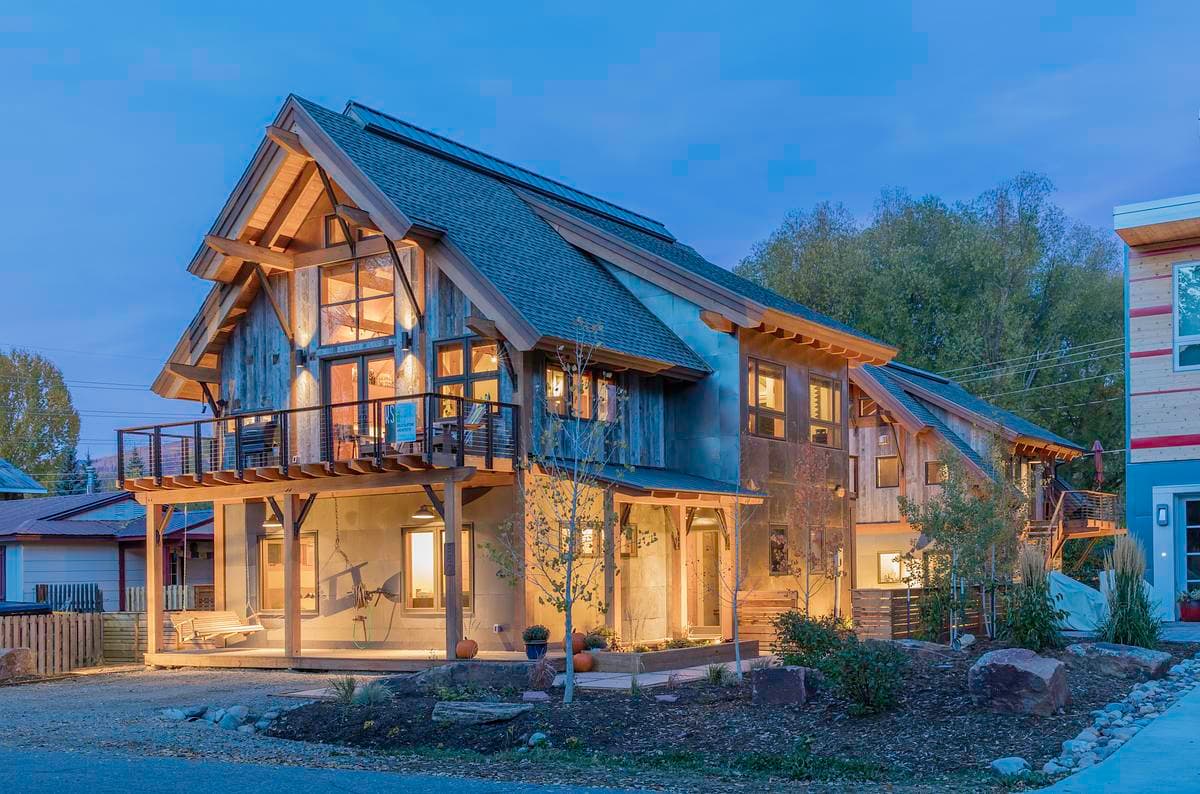 The glazed corner and timber gable illuminate the house at dusk.