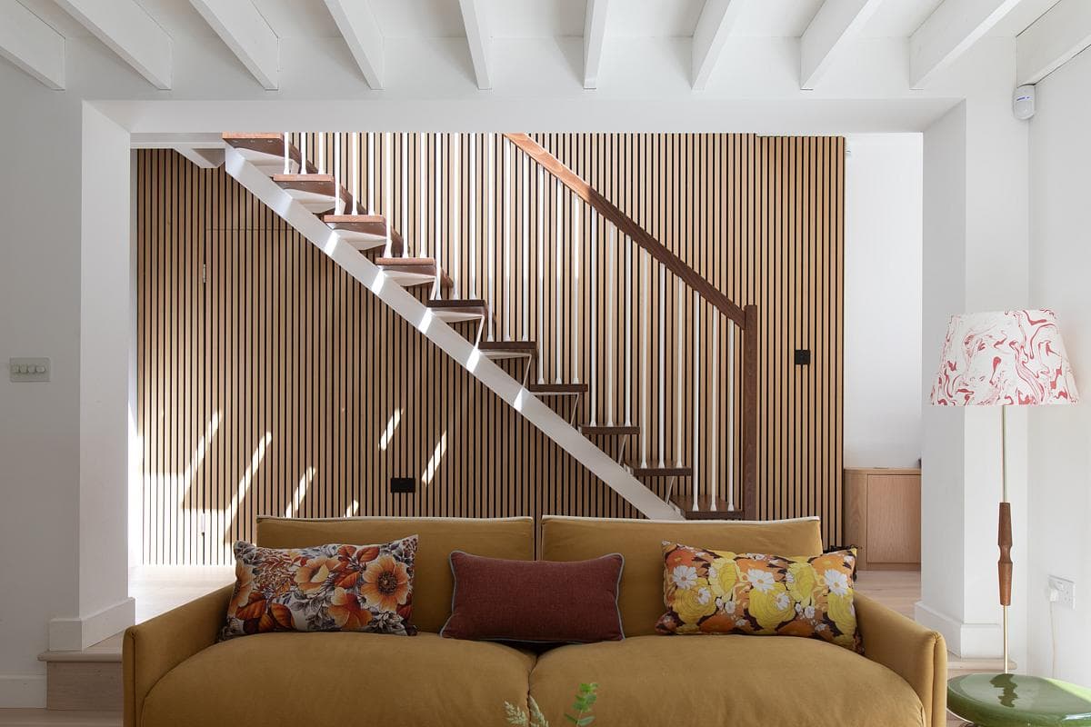 A light stair rises above the sofa beside a timber-screened wall.