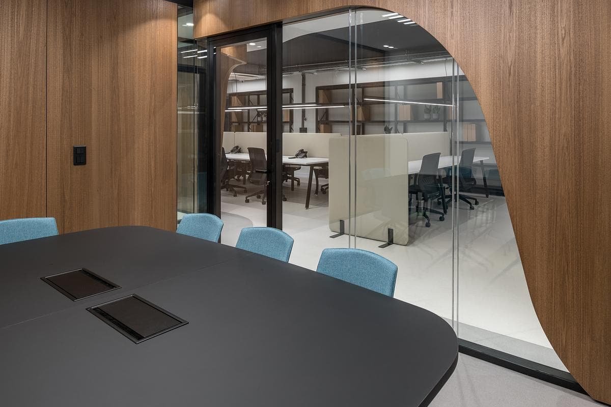 A dark meeting table and blue chairs sit within the glazed room.