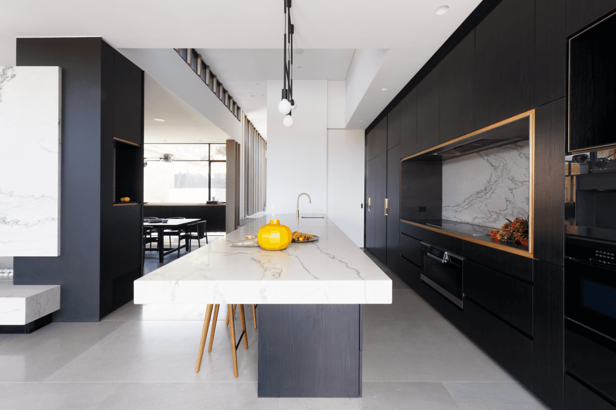 A pale island contrasts with dark kitchen surfaces and stone detailing.