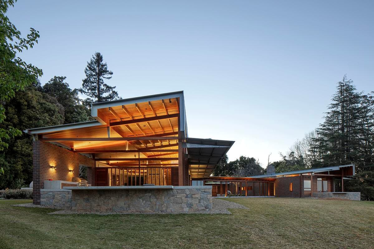 Low roof forms and glazed living spaces seen from the garden at dusk.