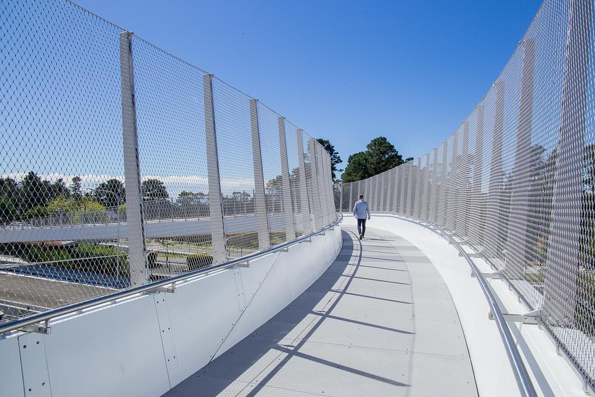 A pedestrian crosses the curved deck between mesh screens.