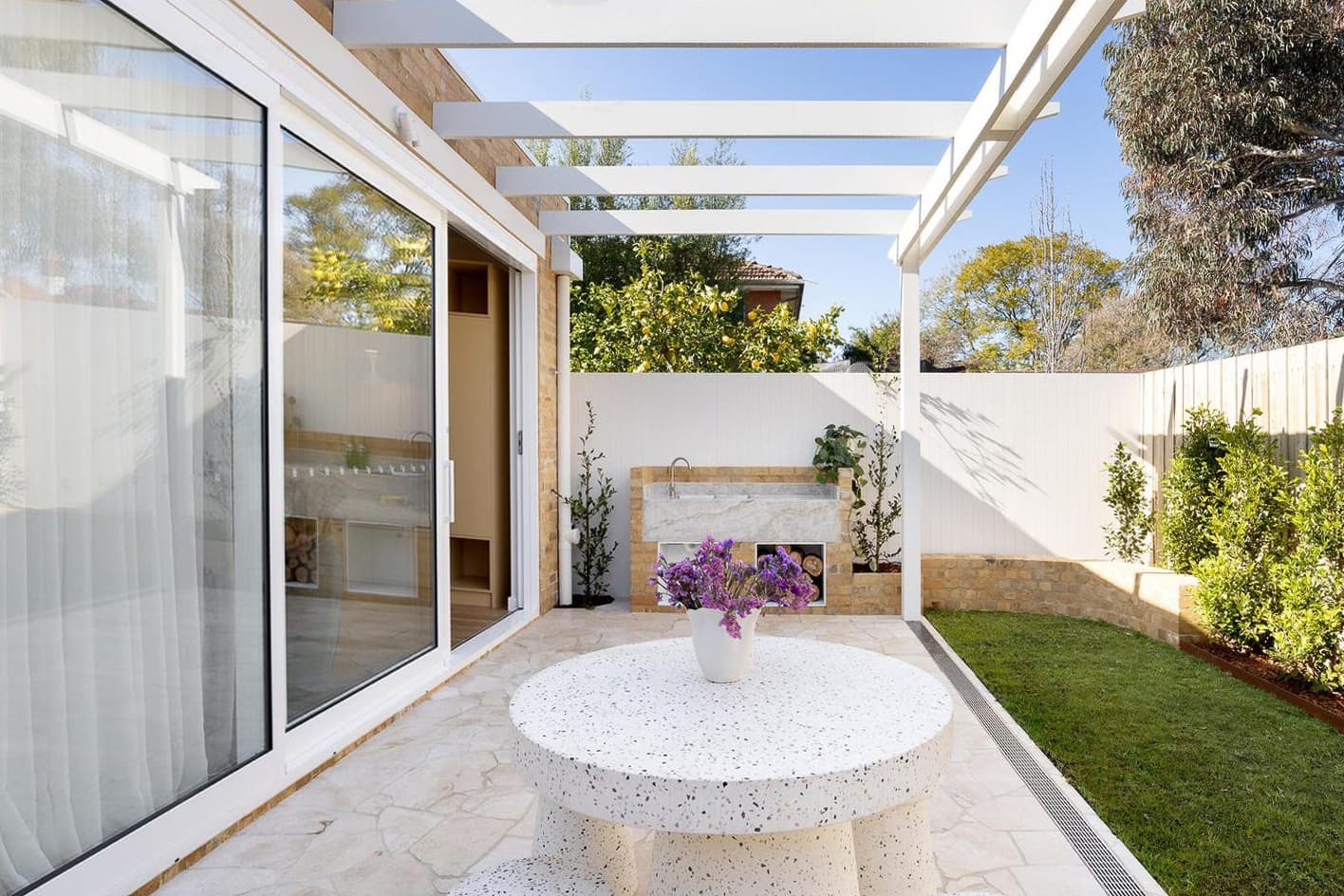 Glazed doors open onto a garden terrace beneath a timber frame.