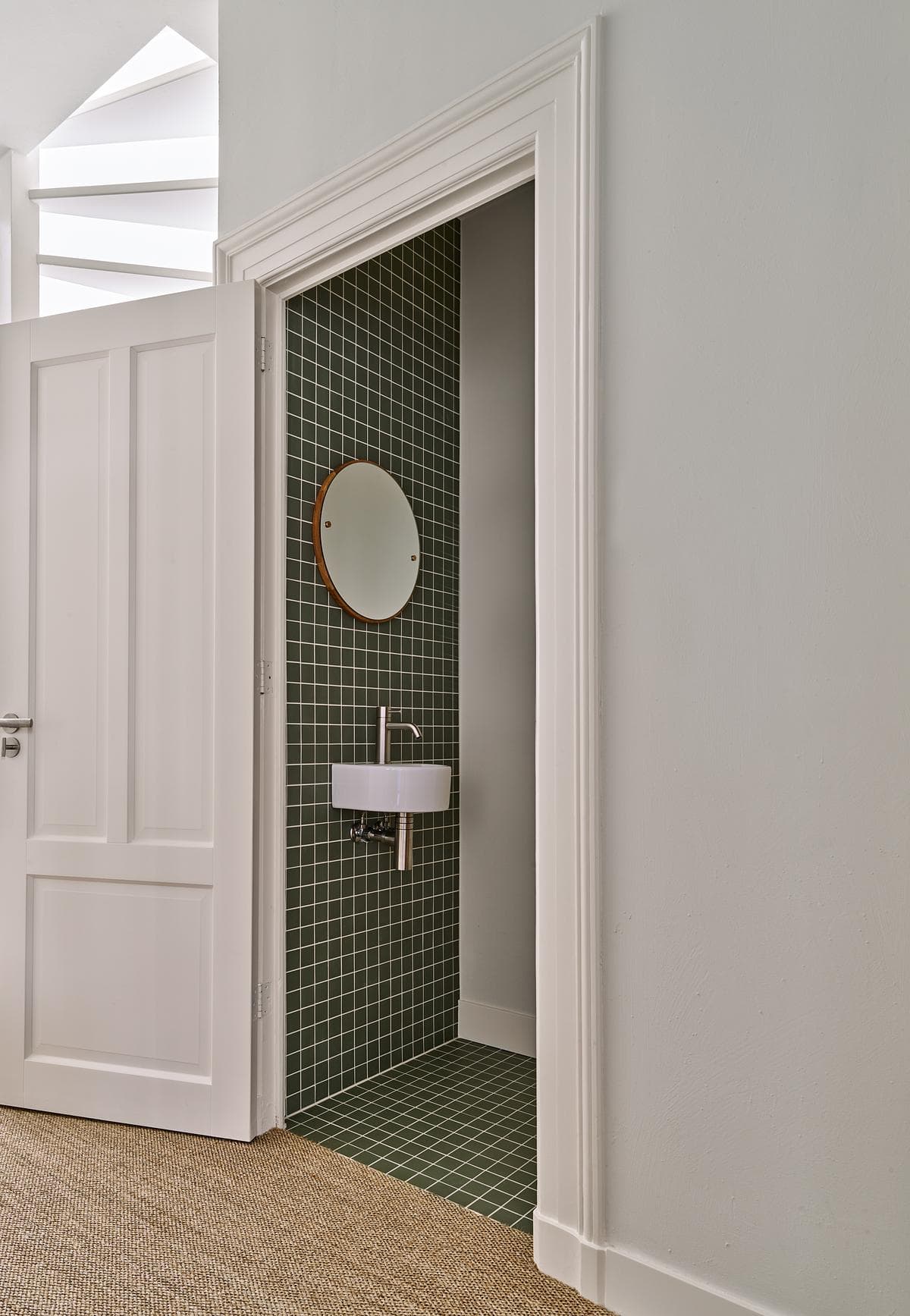 Doorway to a green-tiled washroom with a circular mirror