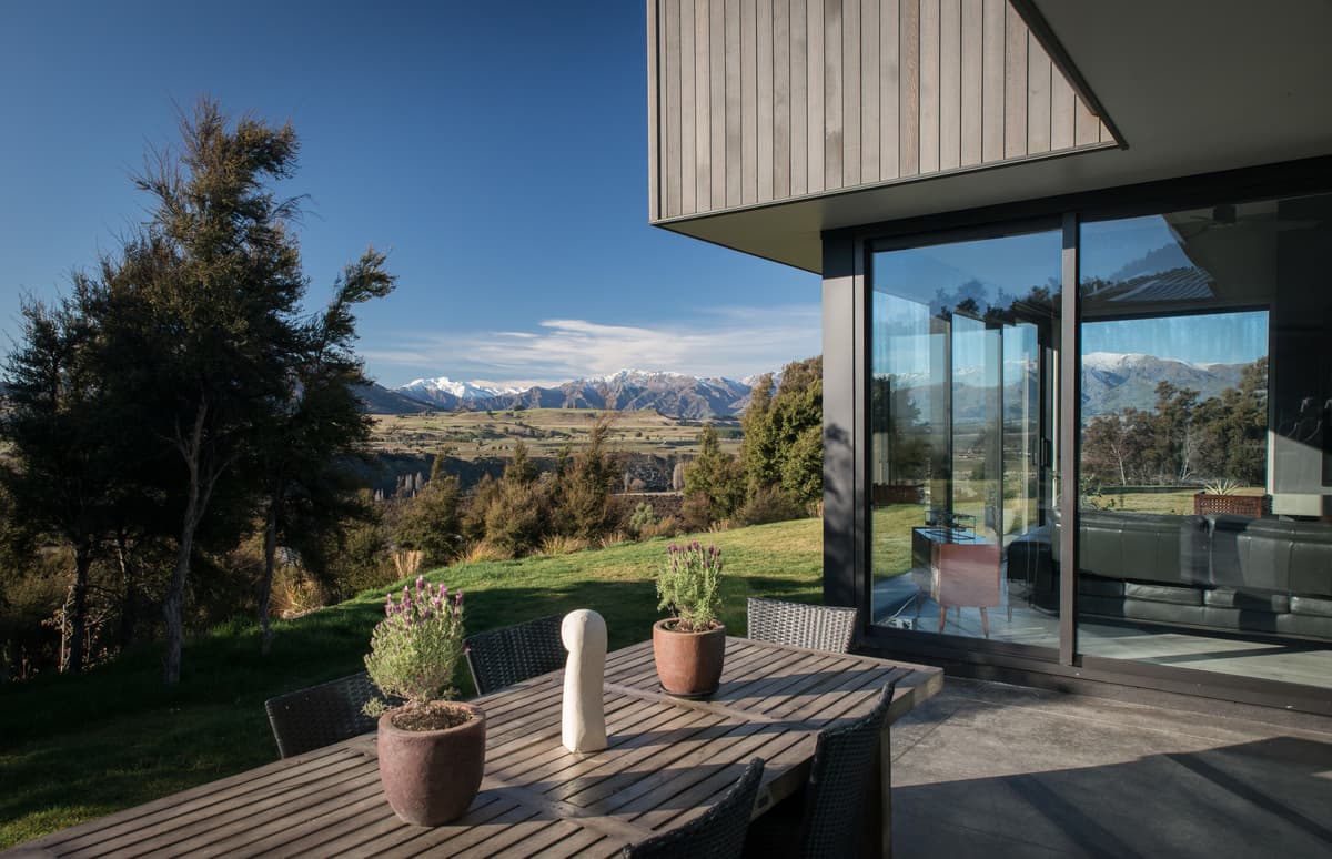 An outdoor table beside glazing that reflects the alpine landscape