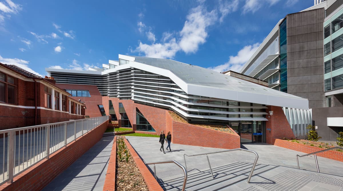 The curved, shaded facade above landscaped terraces and paths by day.