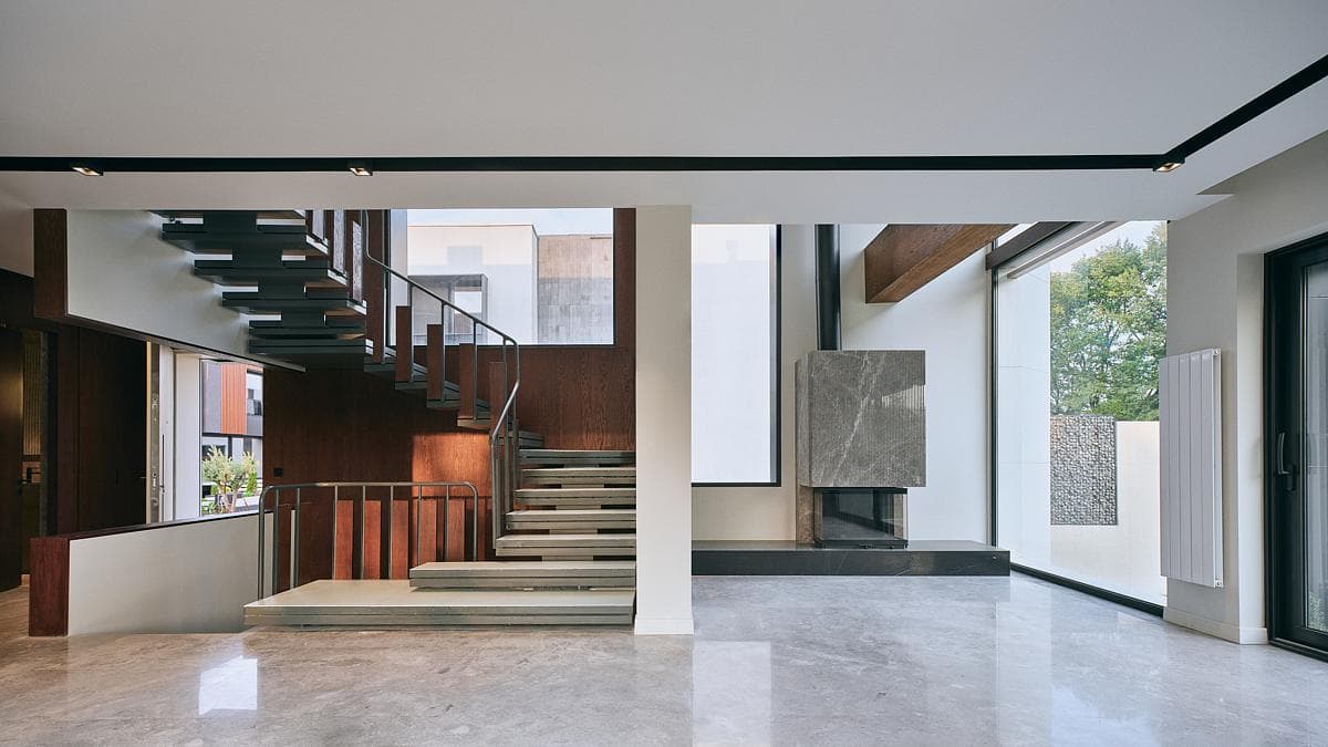 The stair rises through the open interior beside large glazed openings.