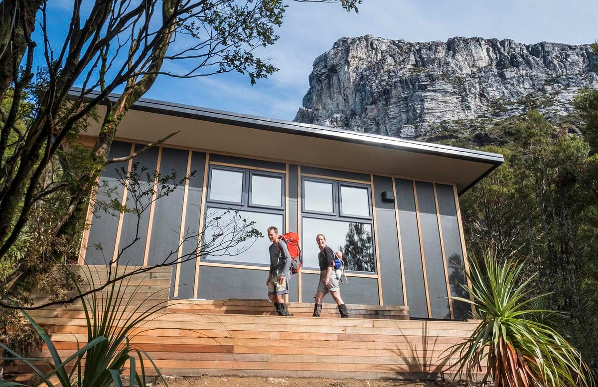The hut’s glazed front and deck sit beneath the quartzite cliffs of Frenchmans Cap.