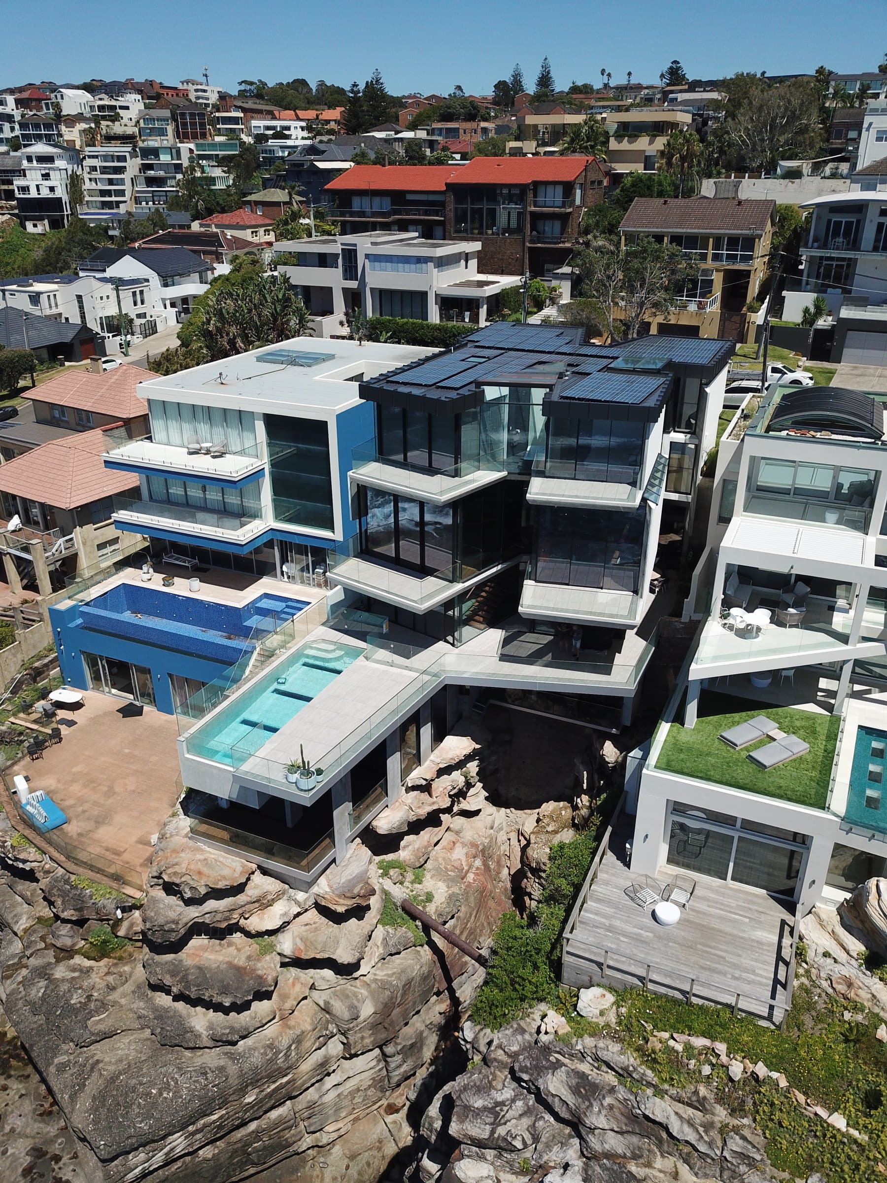 An aerial view shows the house and pool above the rocky coastal ravine.