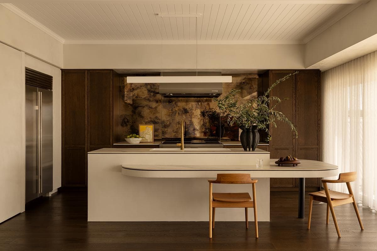 A pale kitchen island sits in front of timber joinery and an exposed stone wall.