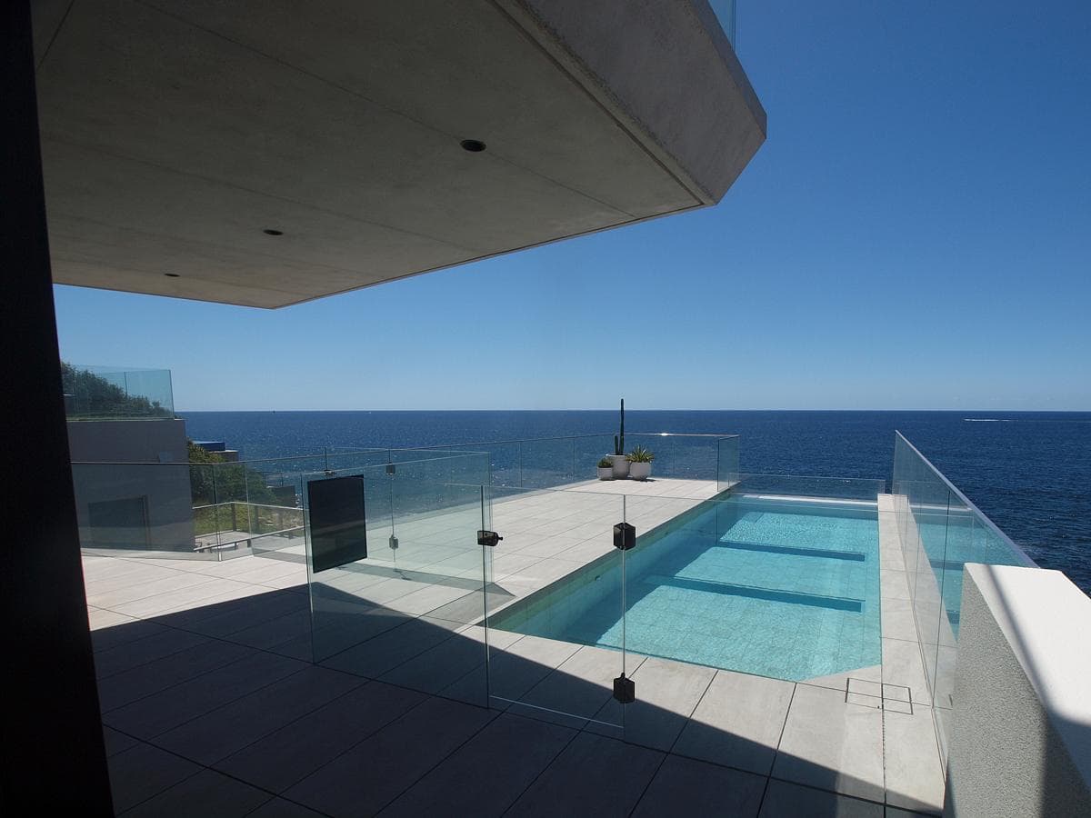 The pool extends towards the ocean beneath a projecting concrete roof.
