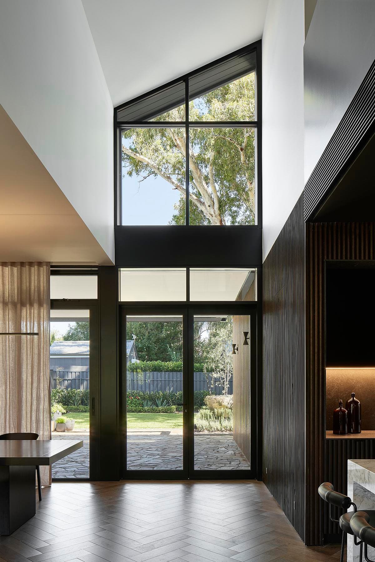 A double-height window frames the trees beyond the living spaces.