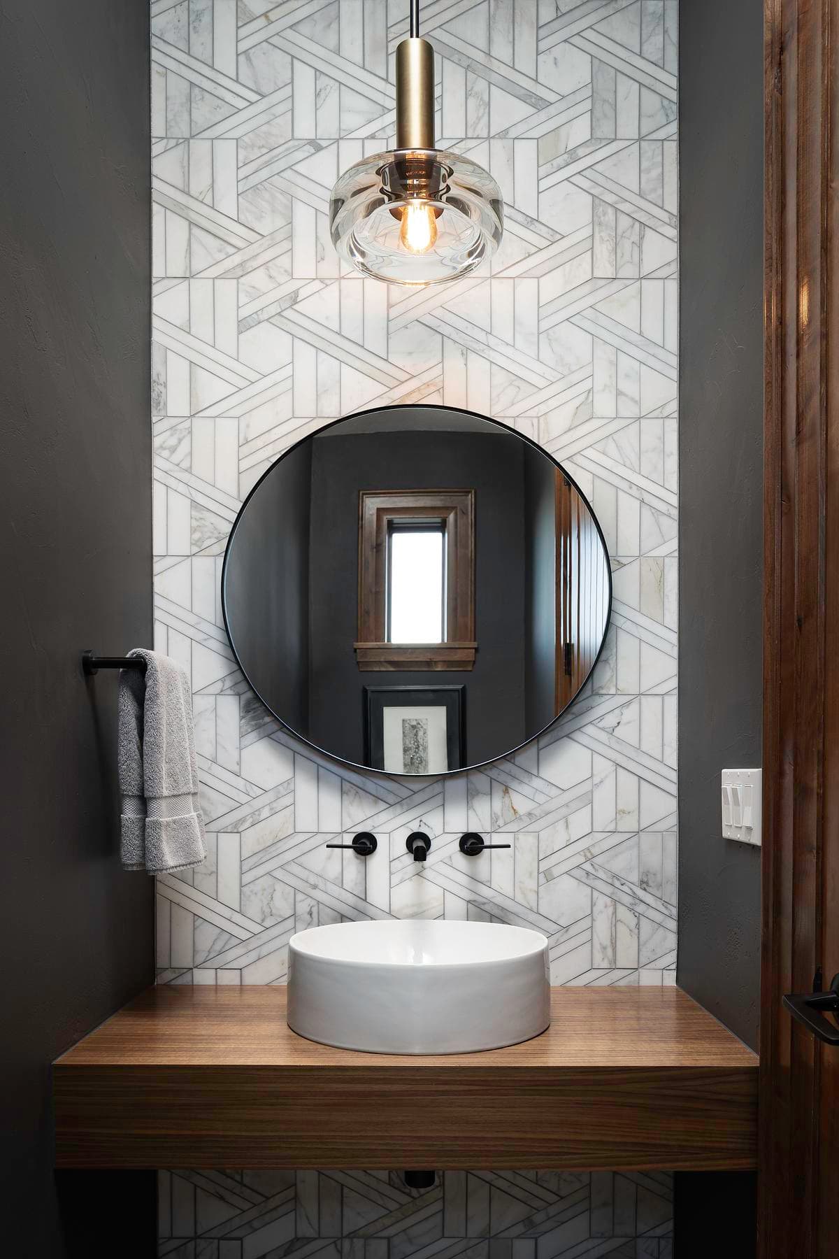 Geometric bathroom tiles and round mirror above a timber vanity