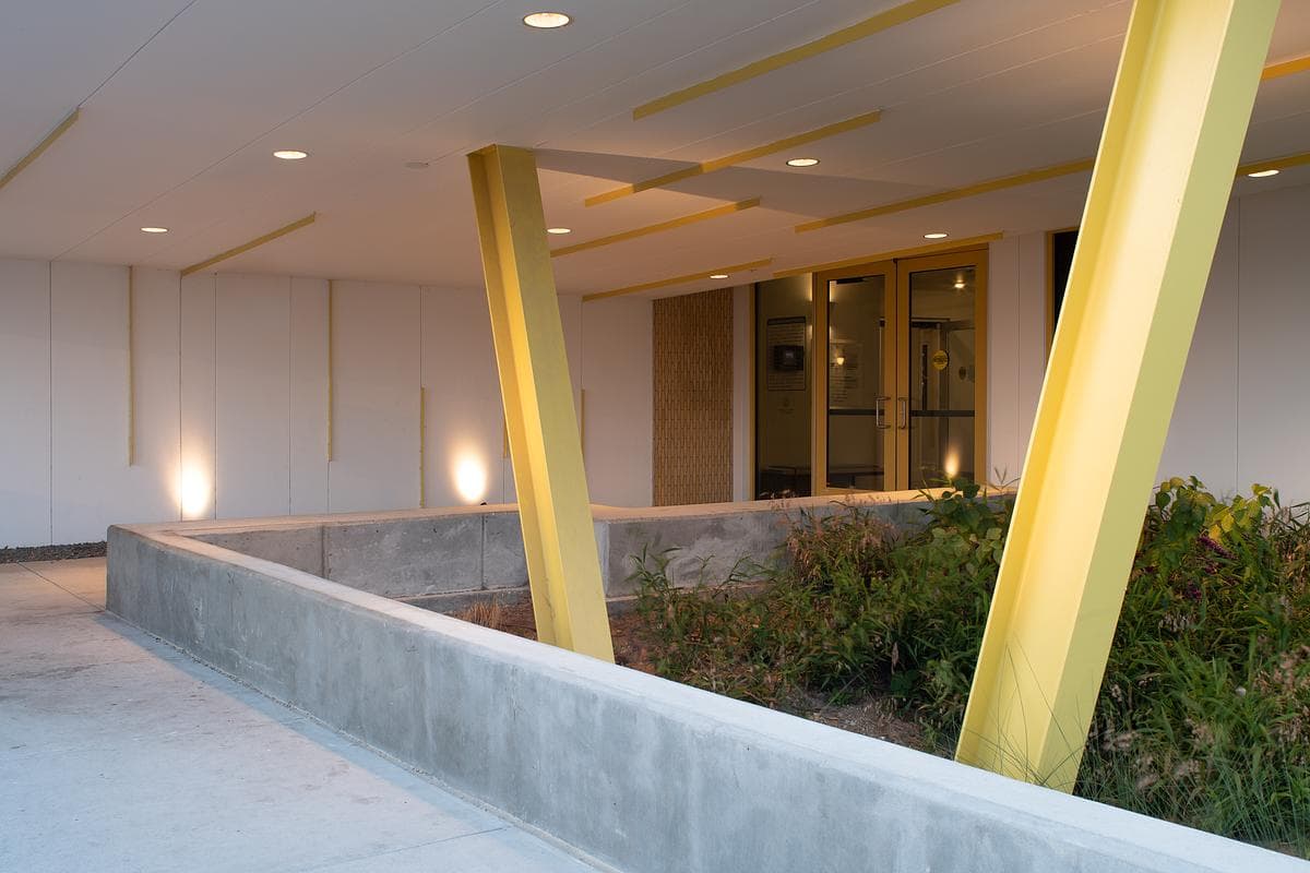 Covered entrance with angled yellow columns and planted edges