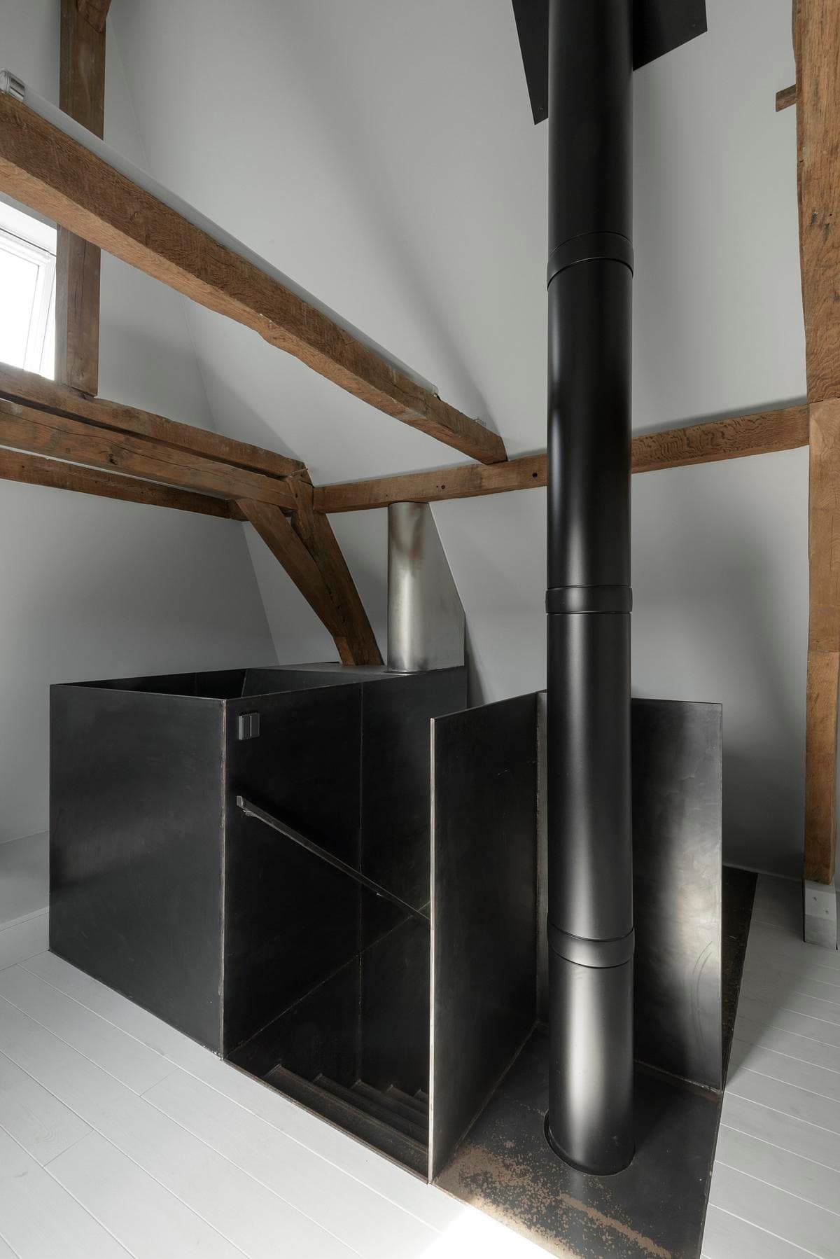 Steel flue and stair core meeting the exposed roof timbers.
