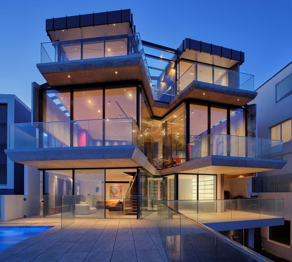 Glazed upper rooms open towards the pool terrace at dusk.