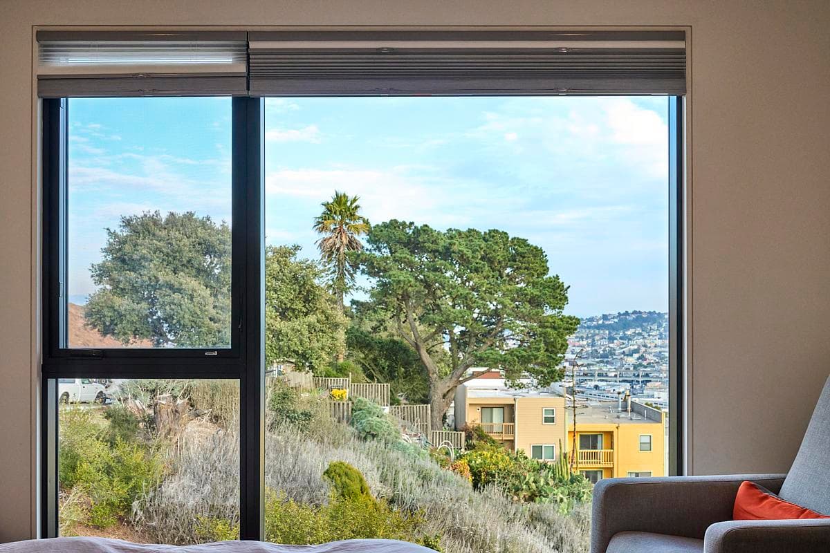 A broad window frames the hillside and city beyond.