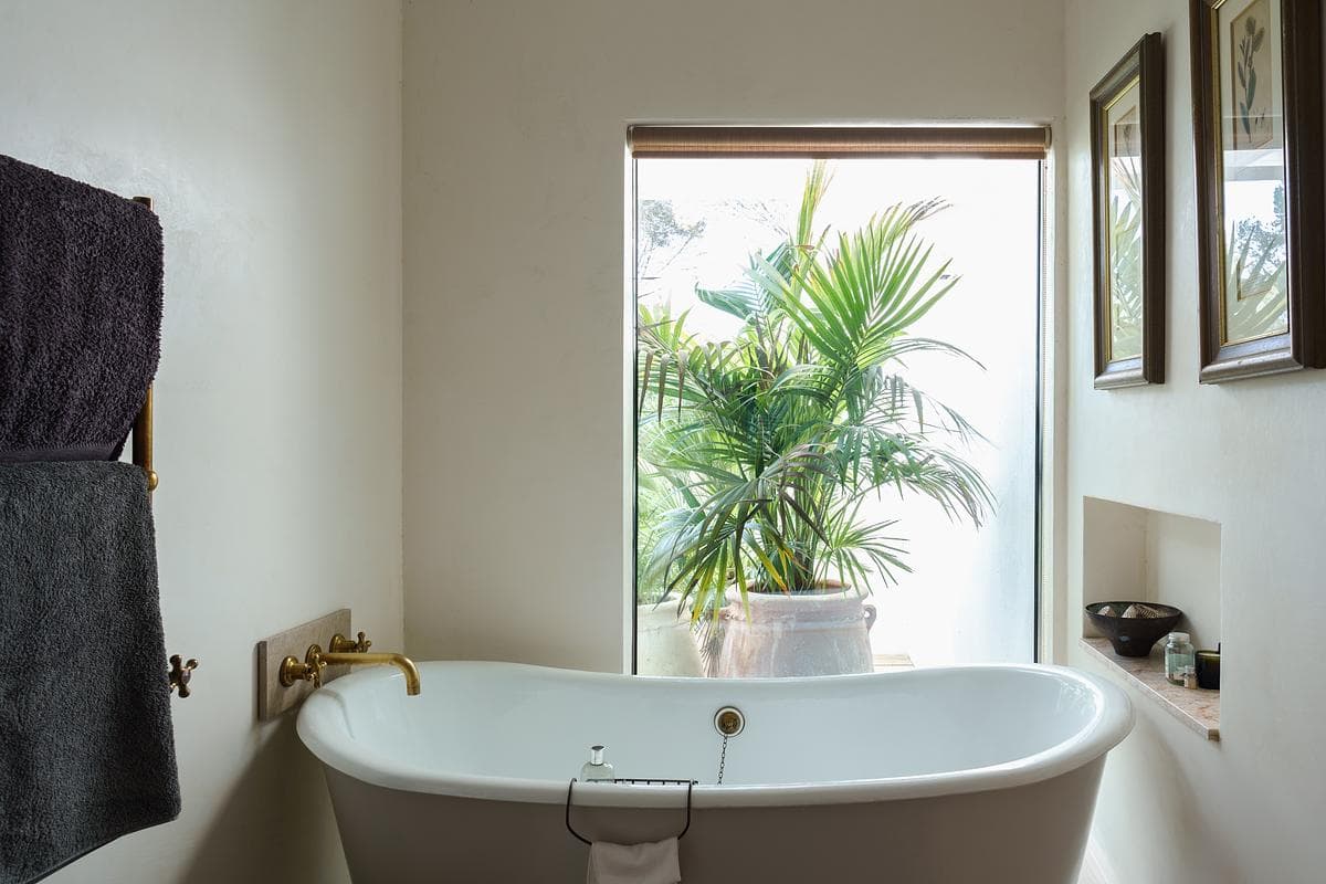 Freestanding bath beside a window and garden planting