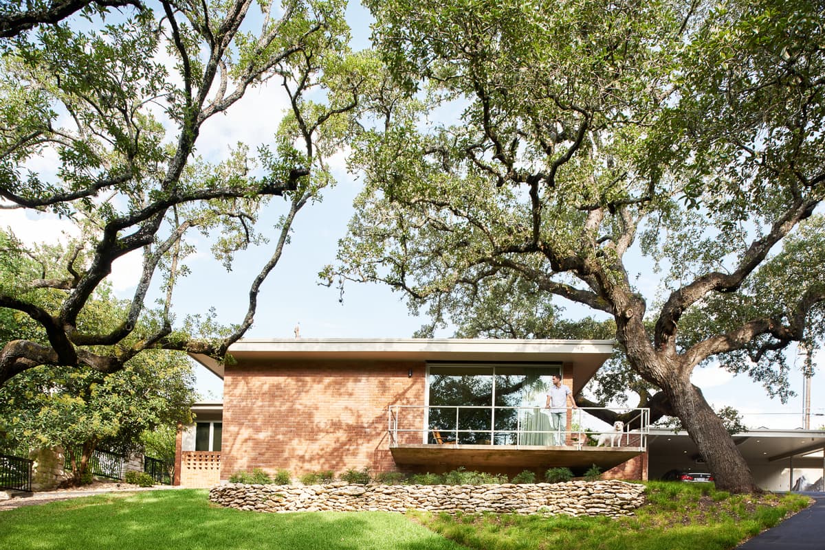The original brick house and cantilevered balcony sit beneath mature trees.