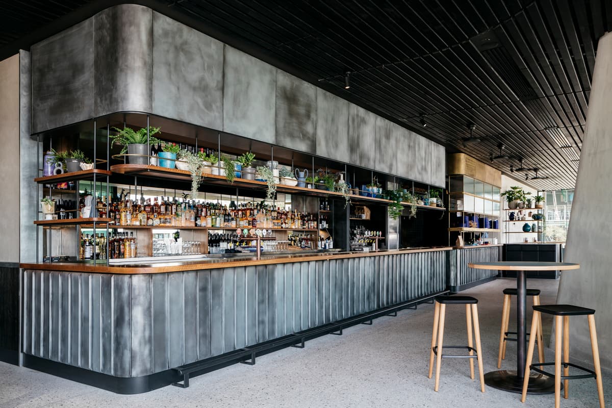 A curved bar brings together dark joinery, timber ceiling battens and the glazed ground-floor edge.
