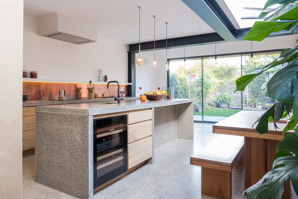 The kitchen combines concrete, plywood joinery and a rooflight above the dining area.